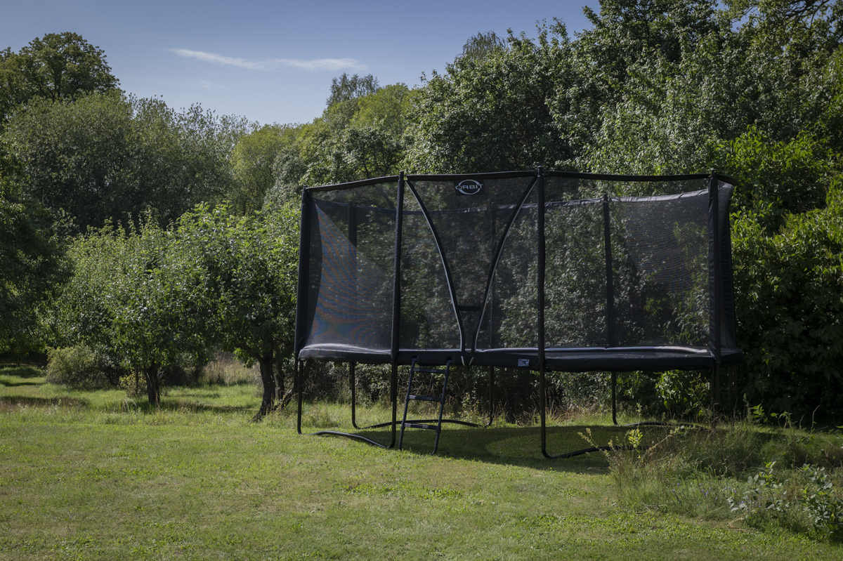 Orbit Stellar Oval studsmatta med skyddsnät monterad i fin trädgård.