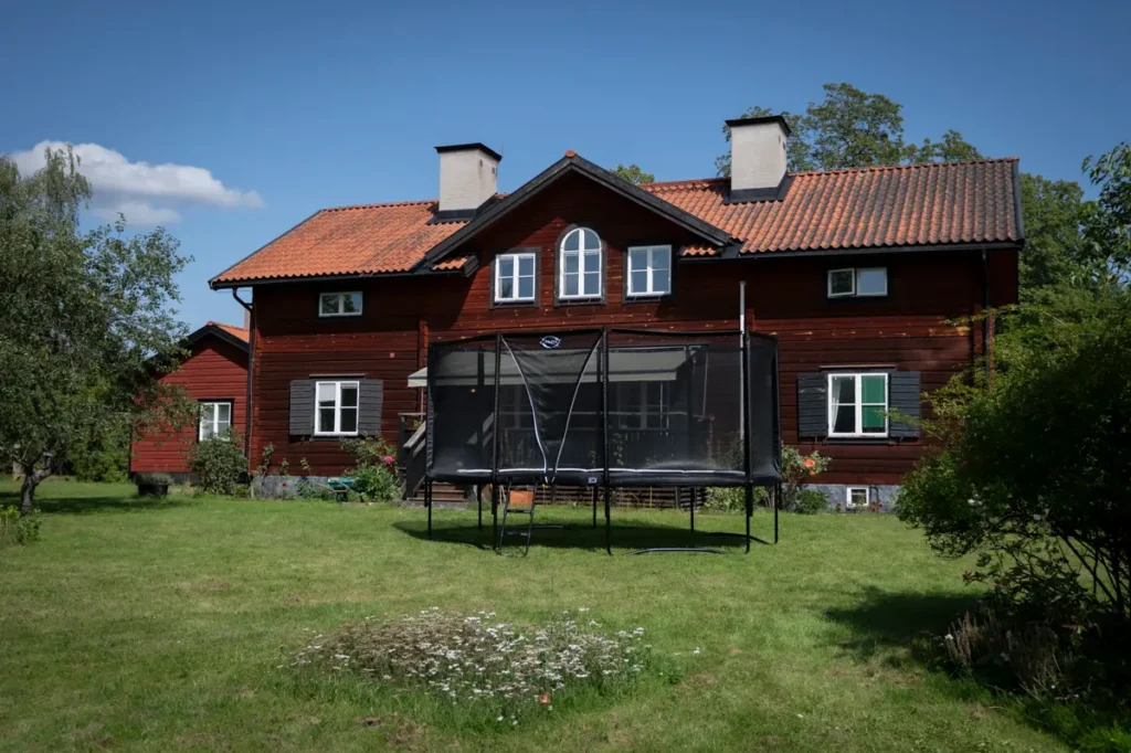 Orbit Stellar Oval studsmatta i grön trädgårdsmiljö framför ett falurött hus.